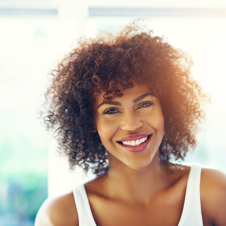 Portrait of young afro-american woman with curly hair looking at camera and smiling on blurred inside background.
