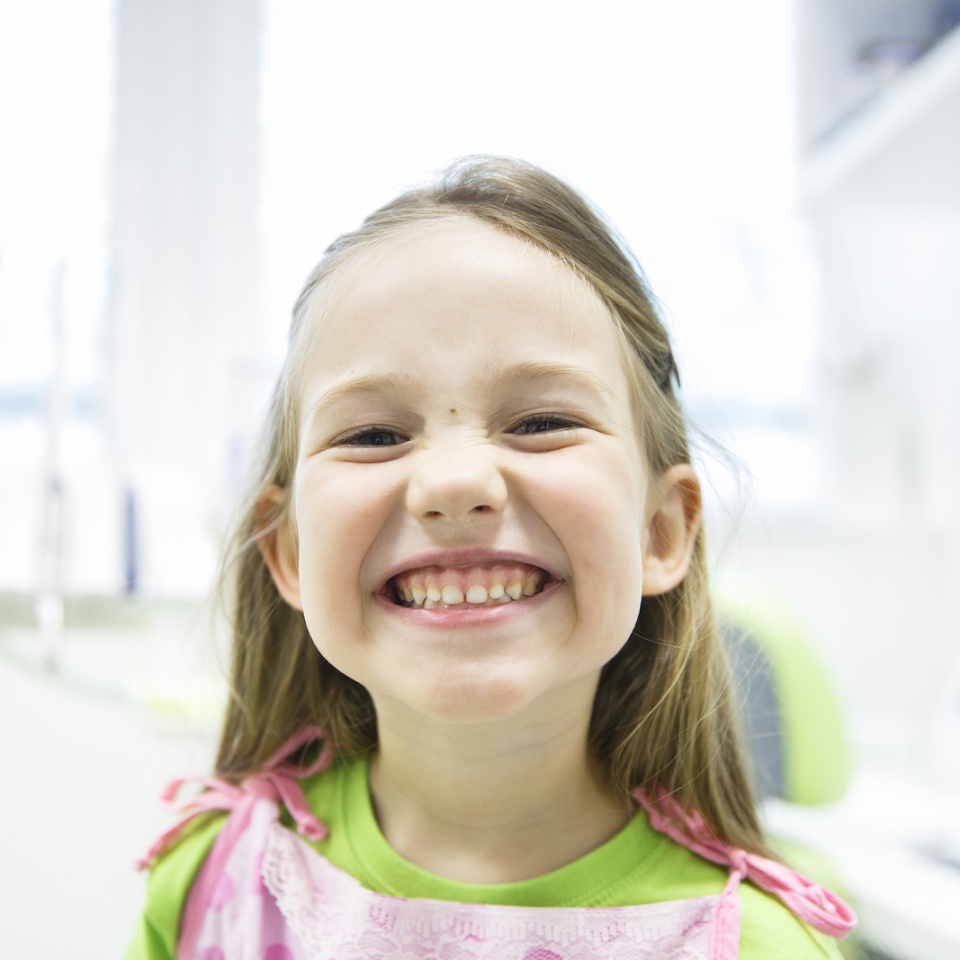 Relaxed little girl showing her healthy milk teeth at dental office smiling and waiting for a checkup. Early prevention paedodontics and no fear concept.