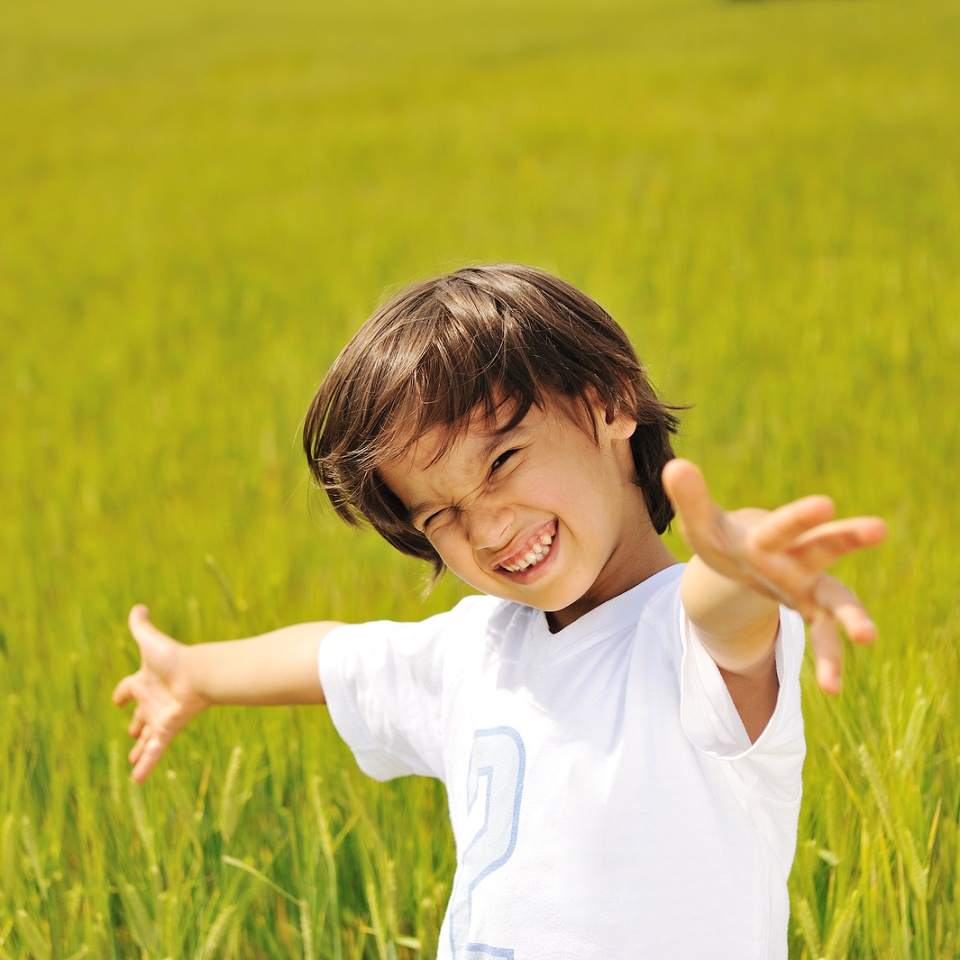 Happy kid on green field with widely opened arms
