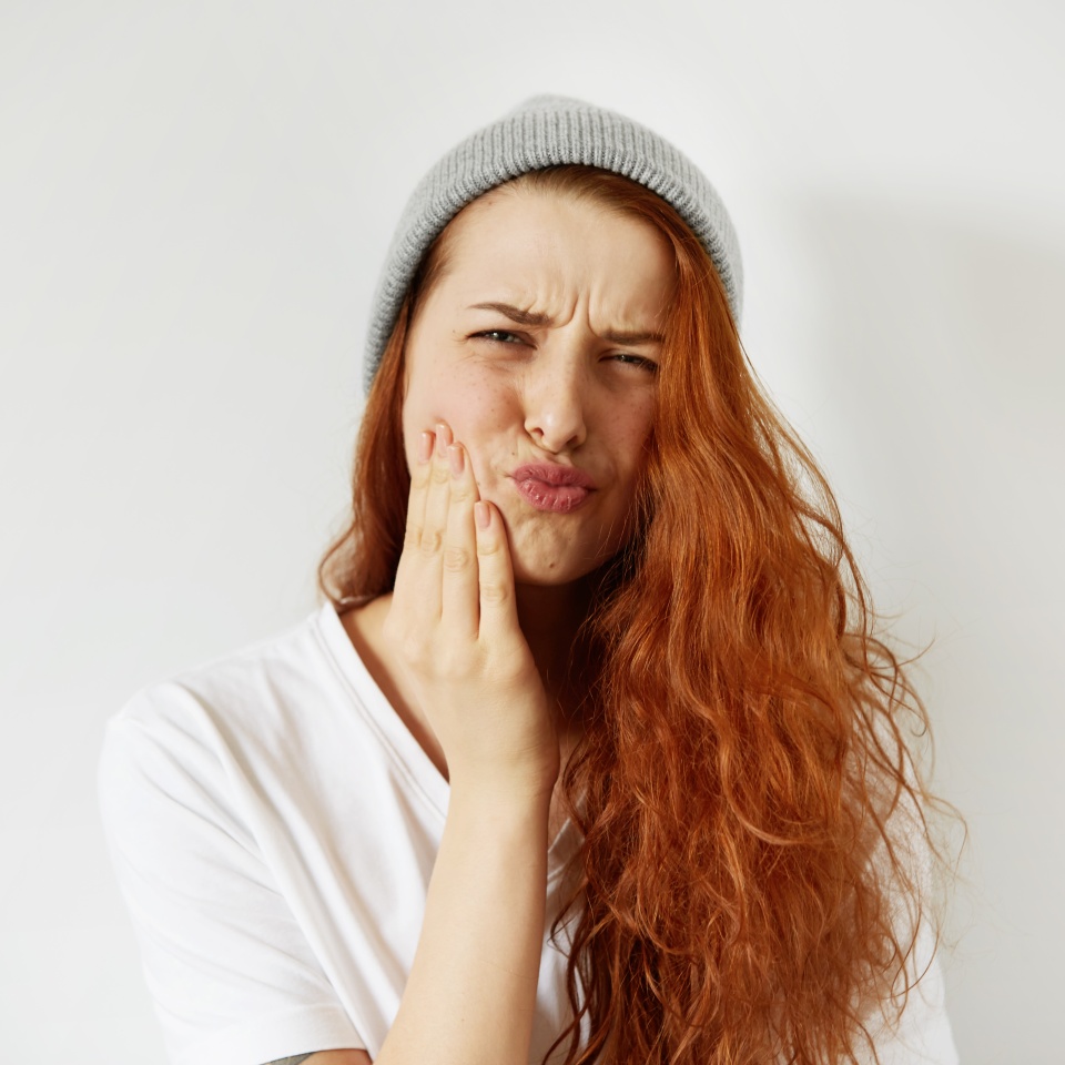 Headshot of redhead teenage woman pressing her cheek with painful expression as if she is having terrible toothache. Negative human emotions face expressions body language. Selective focus