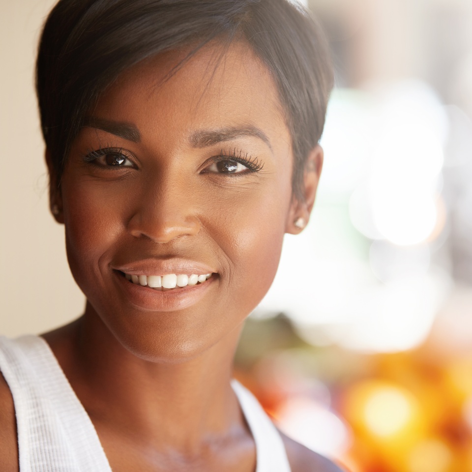 Portrait of beautiful happy young black model with short pixie hairstyle and healthy clean skin looking and smiling at the camera with cheerful expression showing her white teeth posing outdoors