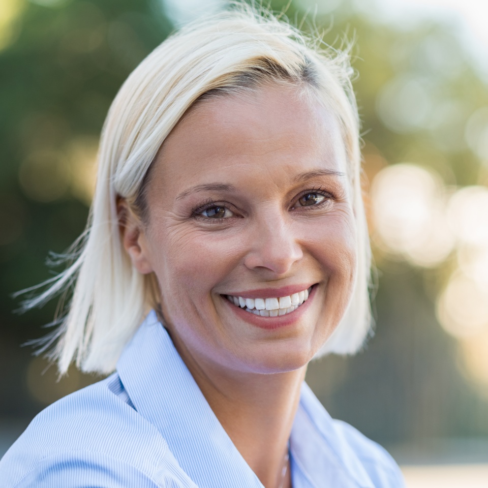 Portrait of mature woman smiling and looking at camera outdoor. Closeup face of a middle aged woman smiling at park. Blond mid woman relaxing in the lawn in a summer day.