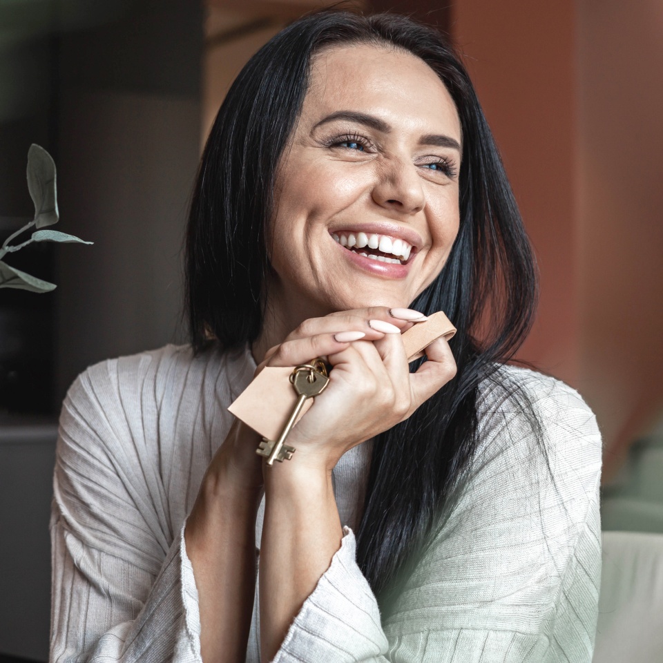 Laughing young brunette woman holding keys from new flat or house enjoying independence with positive emotion. Smiling female with natural beauty owner of apartment celebrating buying purchasing