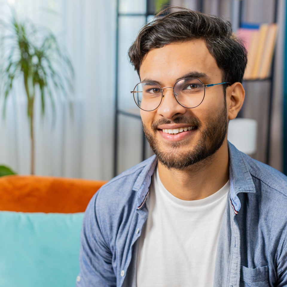 Portrait of happy calm Indian Arab man at home couch smiling friendly glad expression looking away dreaming resting relaxation feel satisfied good news celebrate win. Arabian young guy in living room