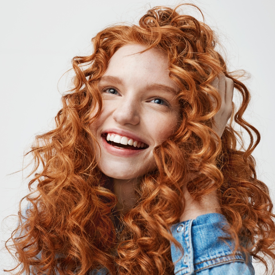 Portrait of cute happy girl smiling touching her curly red hair over white background.
