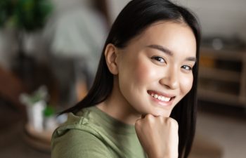 Portrait of young asian woman with clean glowing skin, looking and smiling at camera, sitting at home alone in living room. Lifestyle concept