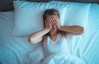 Young stressed woman lying on bed late at night suffering from insomnia, sleep apnea or stress. Top view of depressed girl lying bed. High angle view of awake girl in the middle of the night.